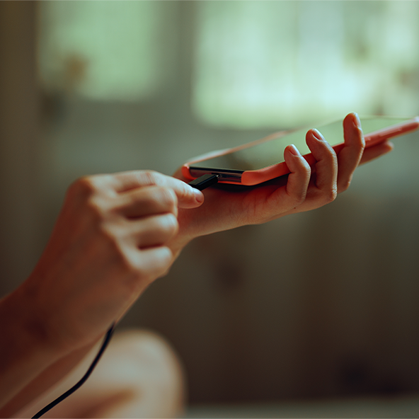 Zdjęcie przedstawia zbliżenie na telefon trzymany w jednym ręku przez kobietę, a drugą dłonią kobieta wpina kabel do ładowania.