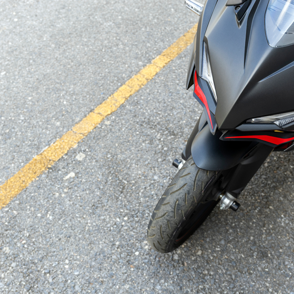 obraz przedstawia fragment motocykla z góry, który stoi na miejscu parkingowym dla motocykli. Obok motocykla widać żółtą linię wyznaczającą krawędź miejsca parkingowego