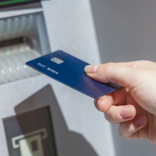 Zbliżenie na granatową kartę płatniczą, którą ktoś trzyma w prawym ręku w próbuje włożyć do bankomatu w Galerii Sudeckiej.