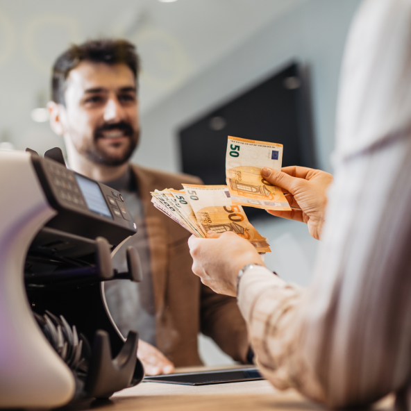 Mężczyzna w średnim wieku, który stoi przy ladzie i wymienia pieniądze w walucie euro.