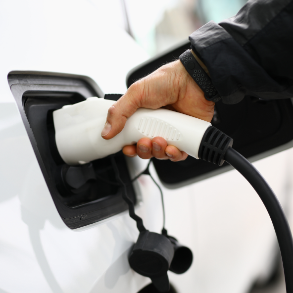 Zbliżenie na ładowarkę samochodów elektrycznych, który trzyma w ręku mężczyzna i ładuje białe auto.