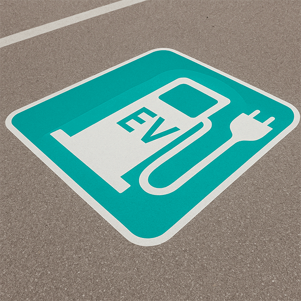 Zdjęcia miejsca parkingowego, a na nim znak poziomy symbolizujący ładowarkę dla auta elektrycznego z napisem EV w kolorze białym na turkusowym tle.