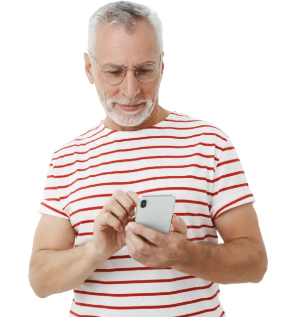 Starszy mężczyzna w siwych włosach i okularach, patrzy na telefon w ręku i przegląda aplikację klubu galerii sudeckiej. Ubrany w tshirt w czerwone paski.